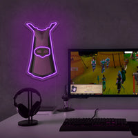 Runescape Thieving Cape neon sign above gaming setup with computer monitor, and headphones on a dark purple wall.